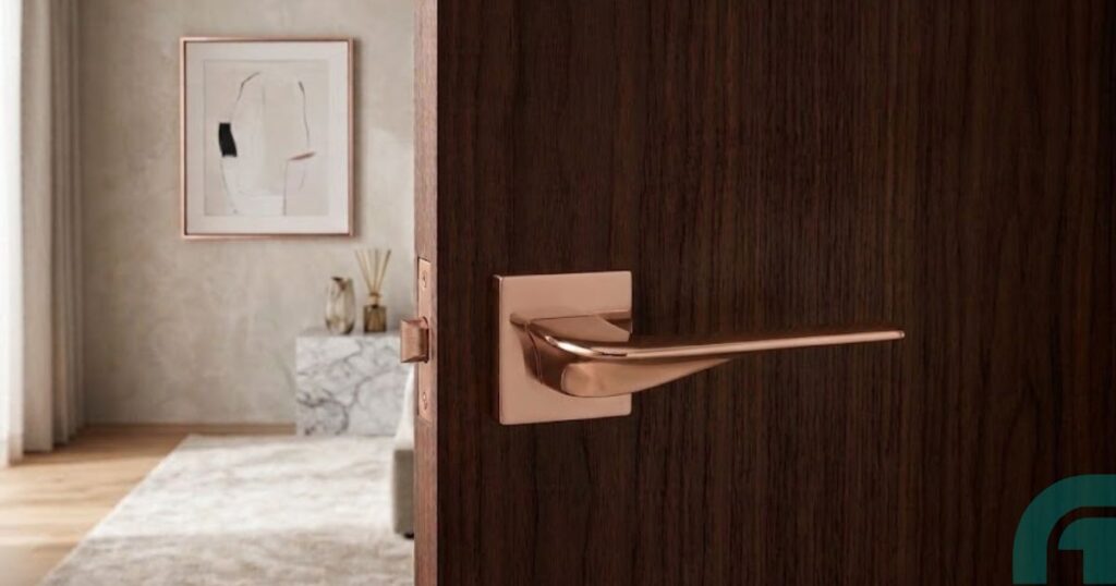 Alloytek - How to Choose the Best Brass Door Handle Manufacturer - Alloytek Close-up of a rose-gold door handle on a dark wood door, opening to a bright, minimalist living room with marble table and abstract art.